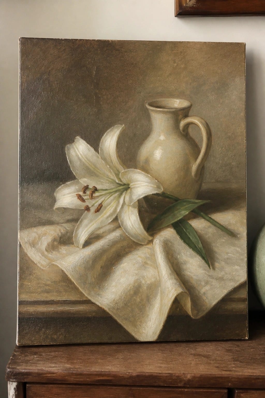 White lily with green leaves beside beige pitcher on draped white cloth