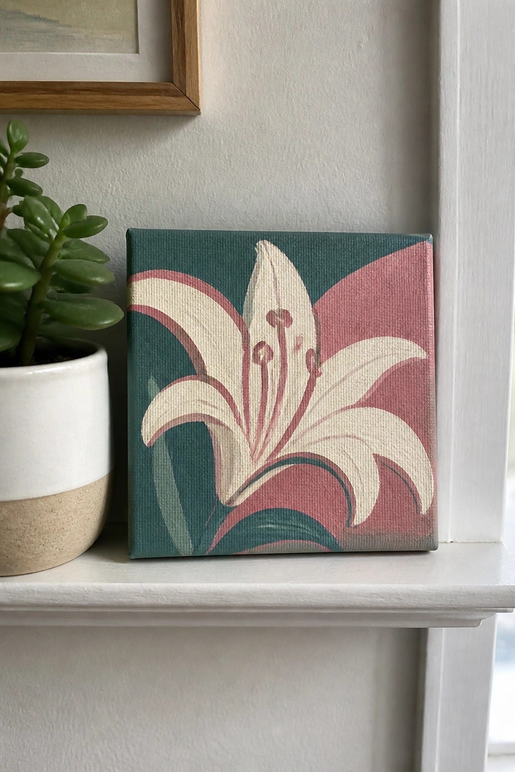 Mini canvas painting of white lily on teal and pink background beside potted plant