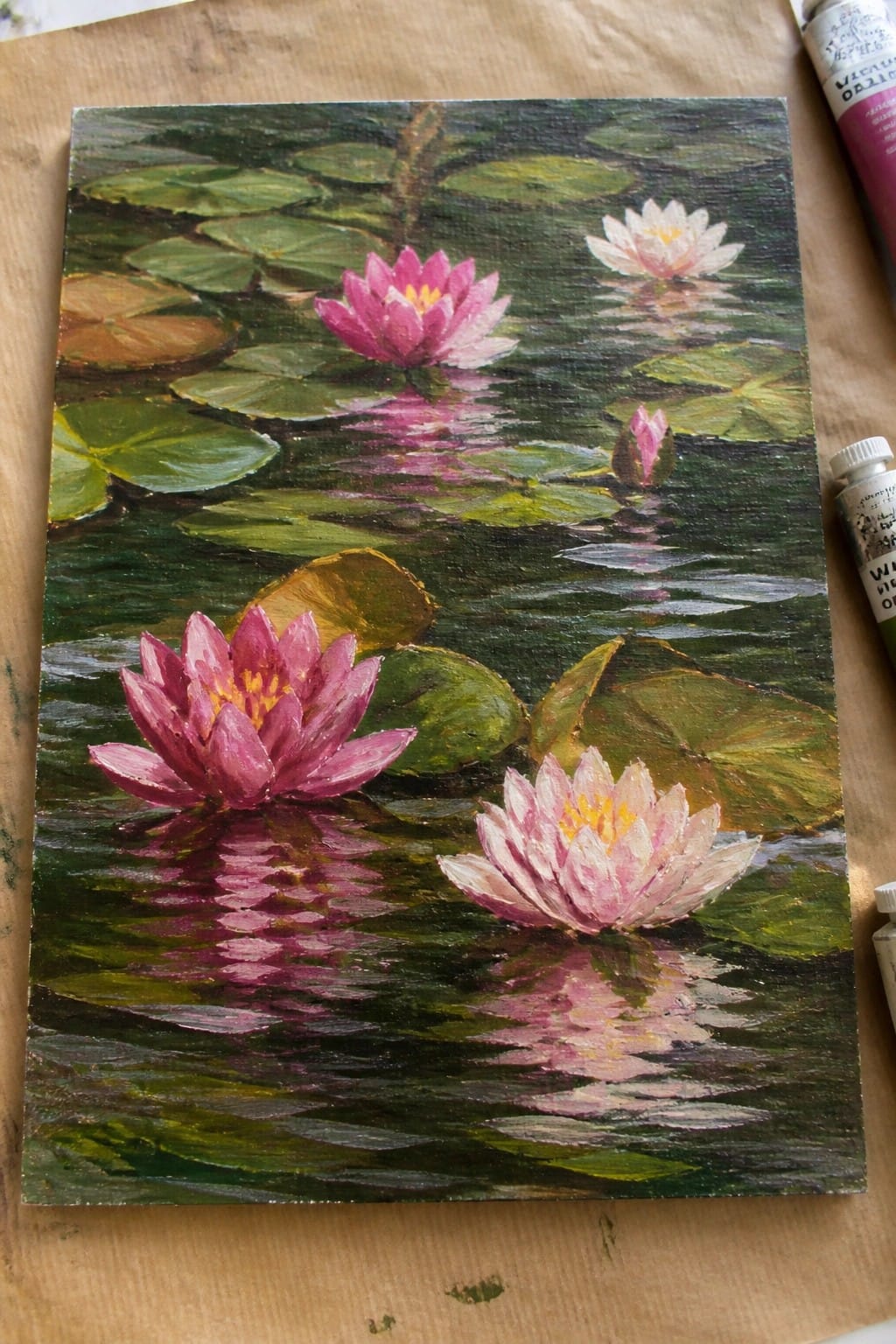 Oil painting of pink water lilies amid green pads with reflections on dark water.