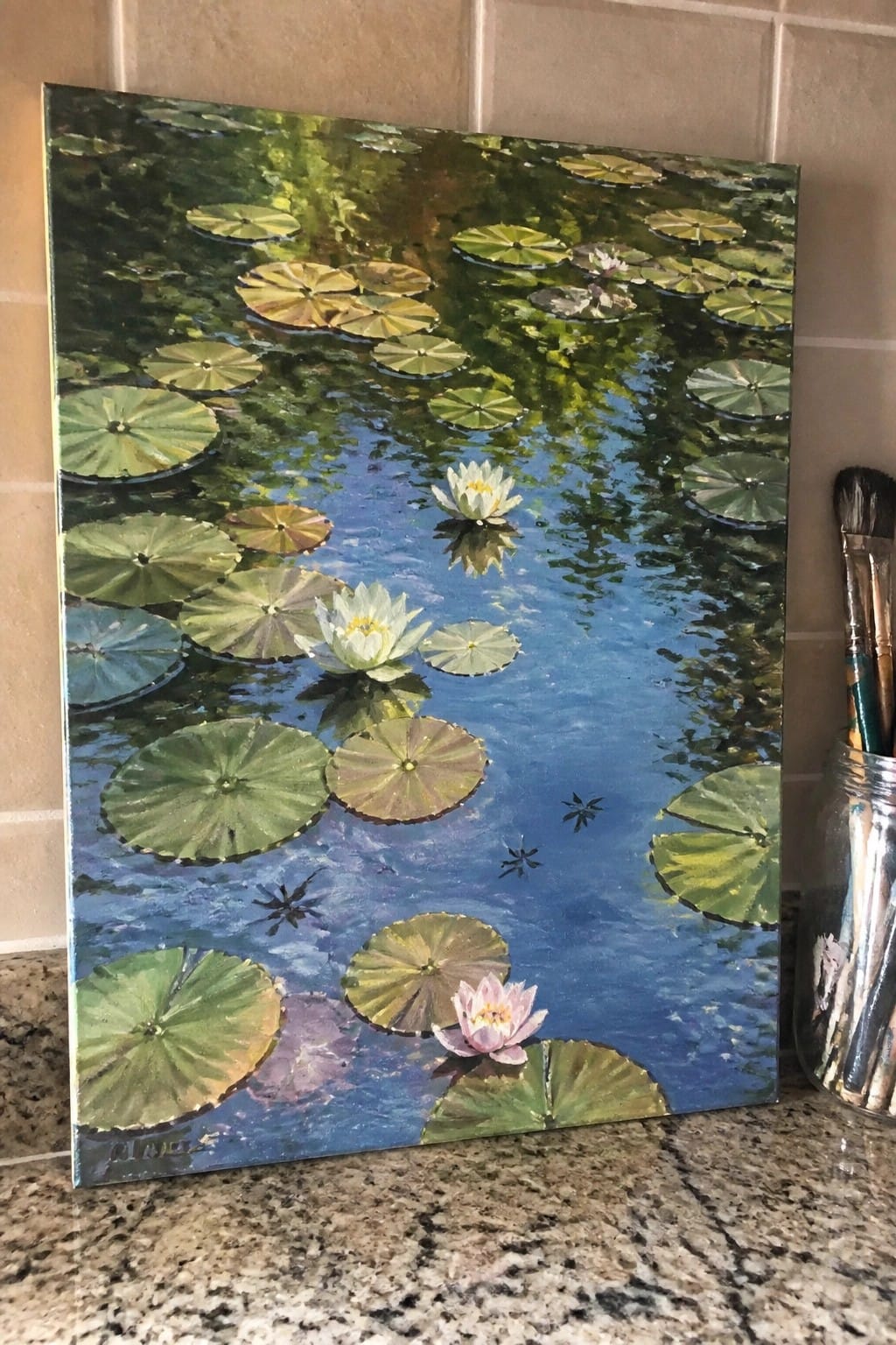 Oil painting of green lily pads and white-pink water lilies on blue pond, paintbrushes nearby
