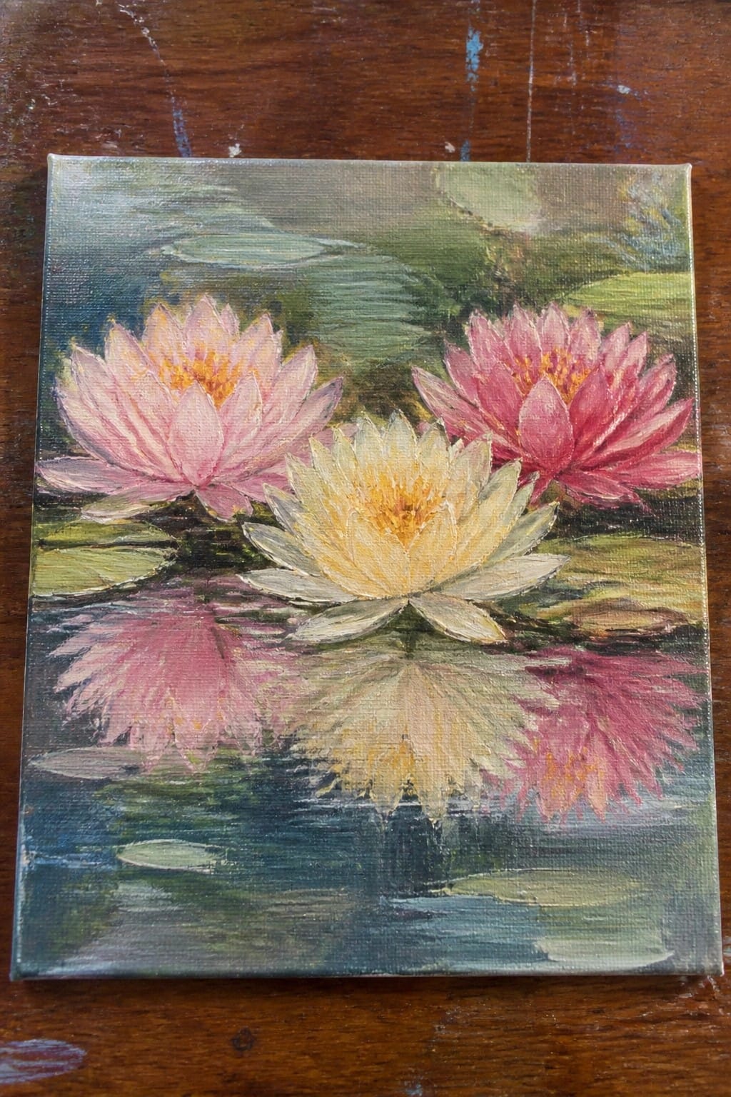 Impressionistic painting of pink and yellow water lilies with reflections on dark water