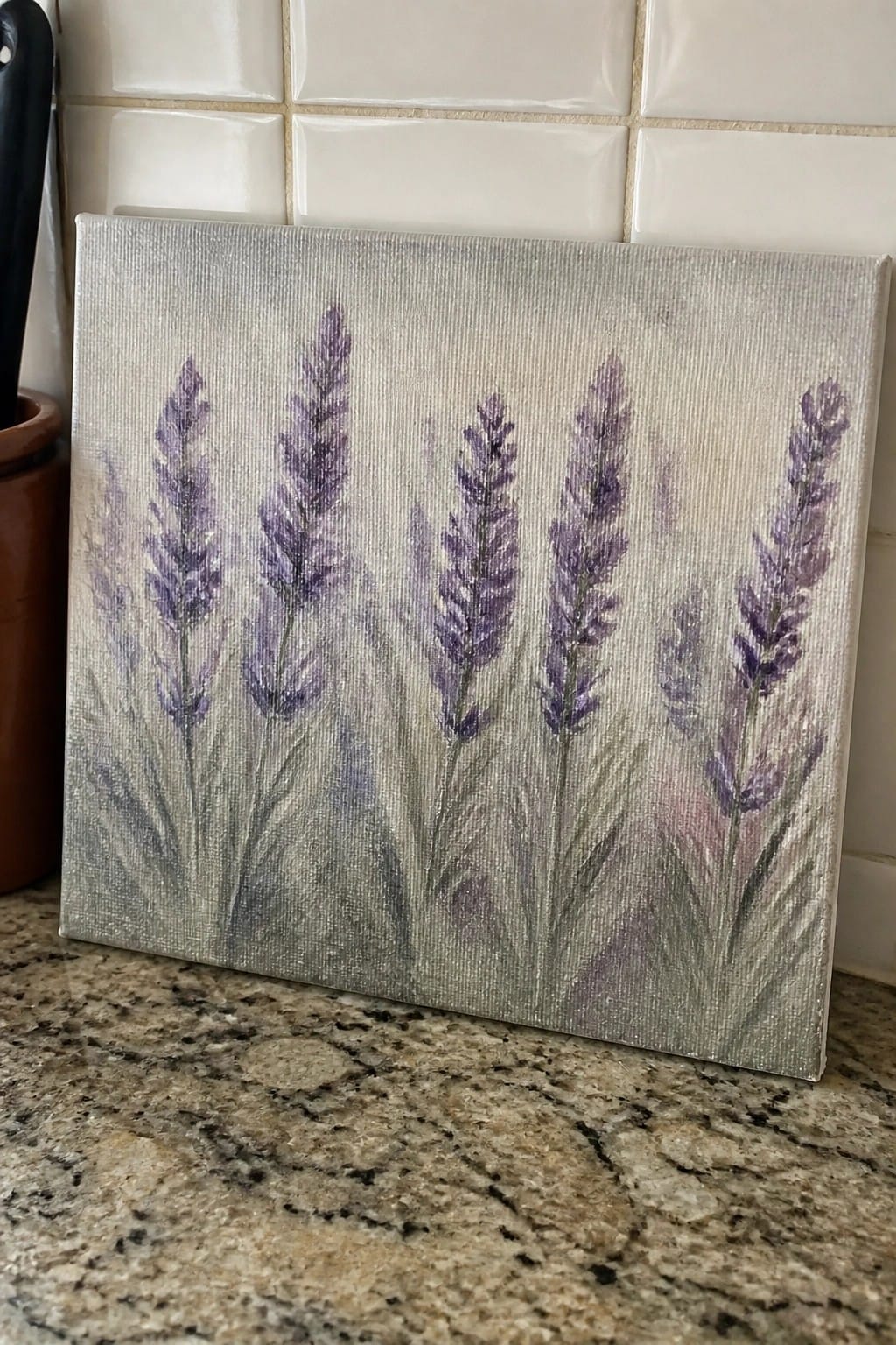 Purple lavender painting on gray canvas leaning on granite counter by tiled wall
