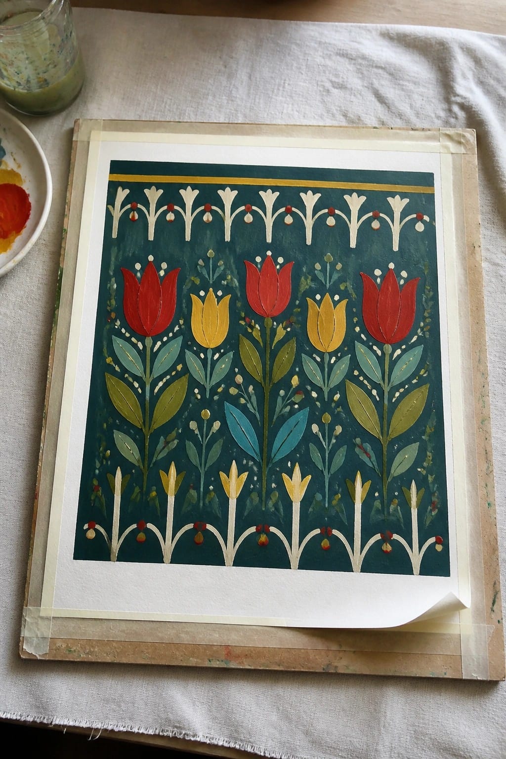 Folk-style painting of red and yellow tulips on teal background with paint supplies nearby.