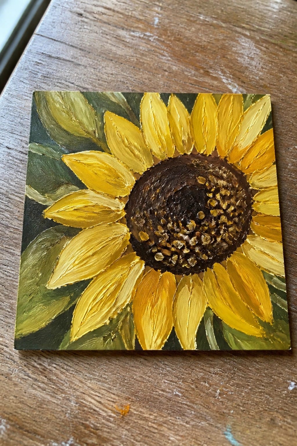 Sunflower painting with yellow petals, dark brown center on wooden table.
