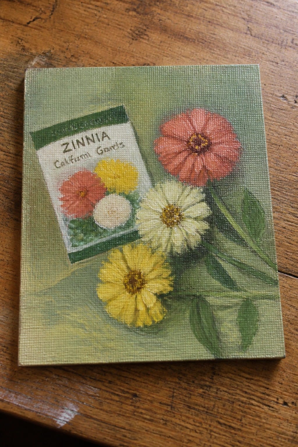 Canvas painting of zinnia seed packet with red, yellow, and white flowers on wood