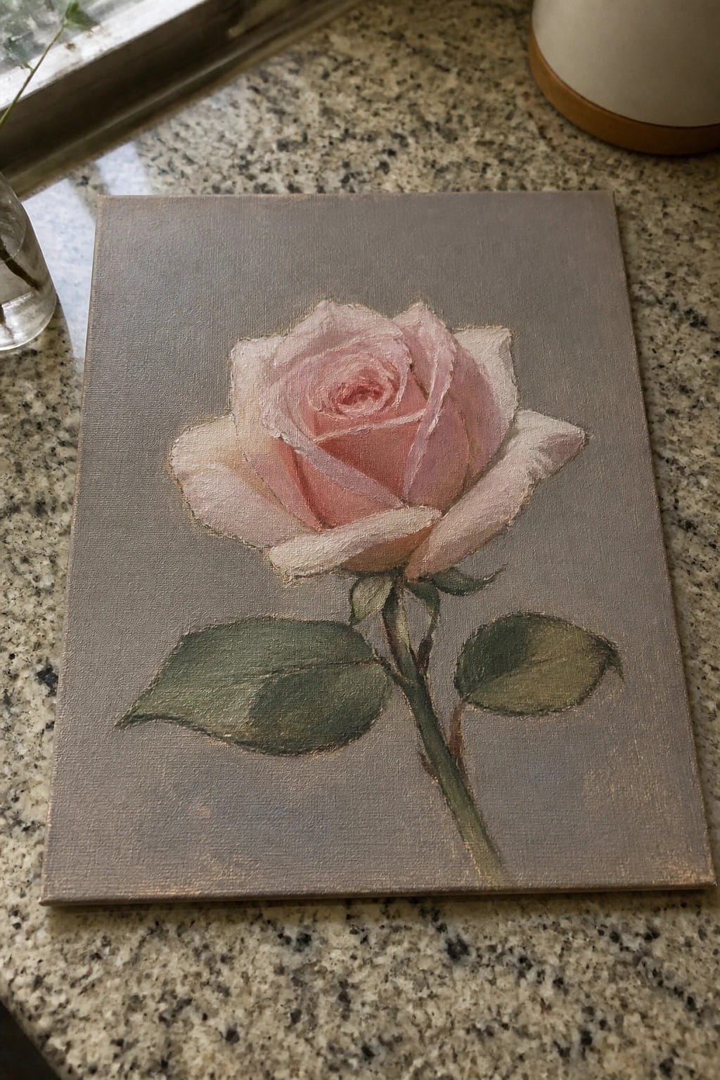Pink rose painting on canvas atop speckled granite kitchen countertop with leaves