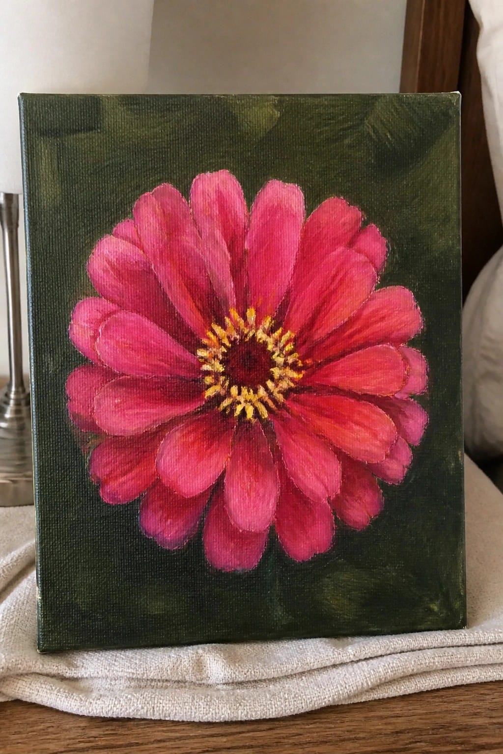An oil painting of a large pink flower with yellow center on a dark green canvas background.