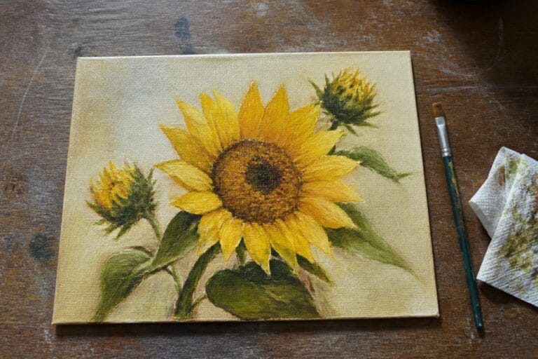 Large yellow sunflower painting on canvas with brush and rag on wood table