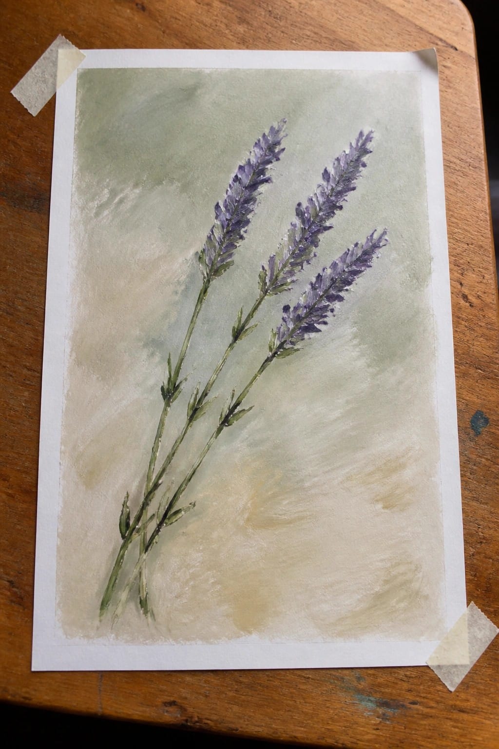 Watercolor painting of three purple lavender stems on green-beige background, taped to wood