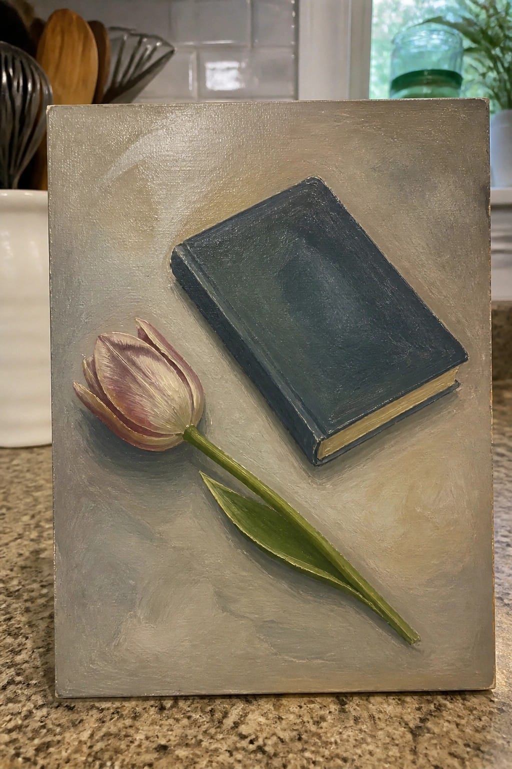 Still life painting of a blue book beside a pink tulip on gray background