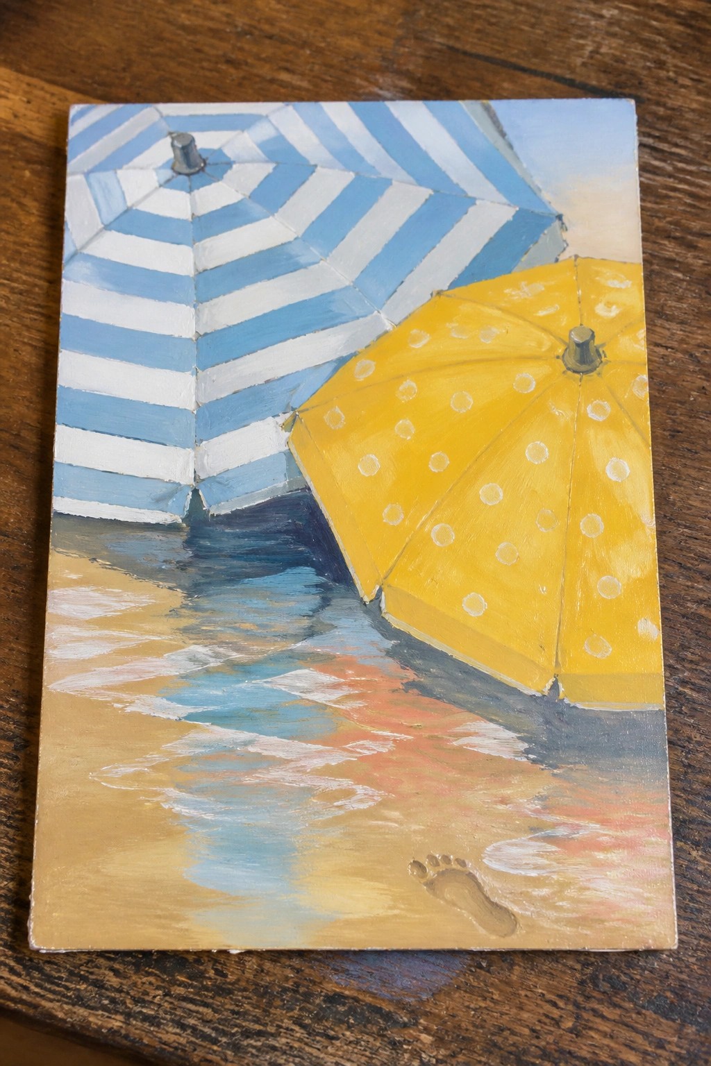 Blue striped and yellow polka-dot umbrellas on beach with footprint in sand.