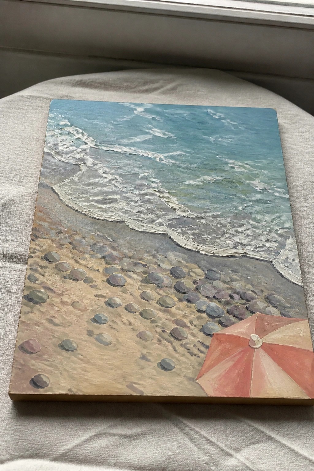 Painting of turquoise waves on pebbled beach with red striped umbrella in corner.