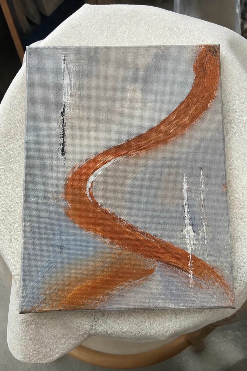 Abstract painting with curved orange stroke on gray canvas over white cloth