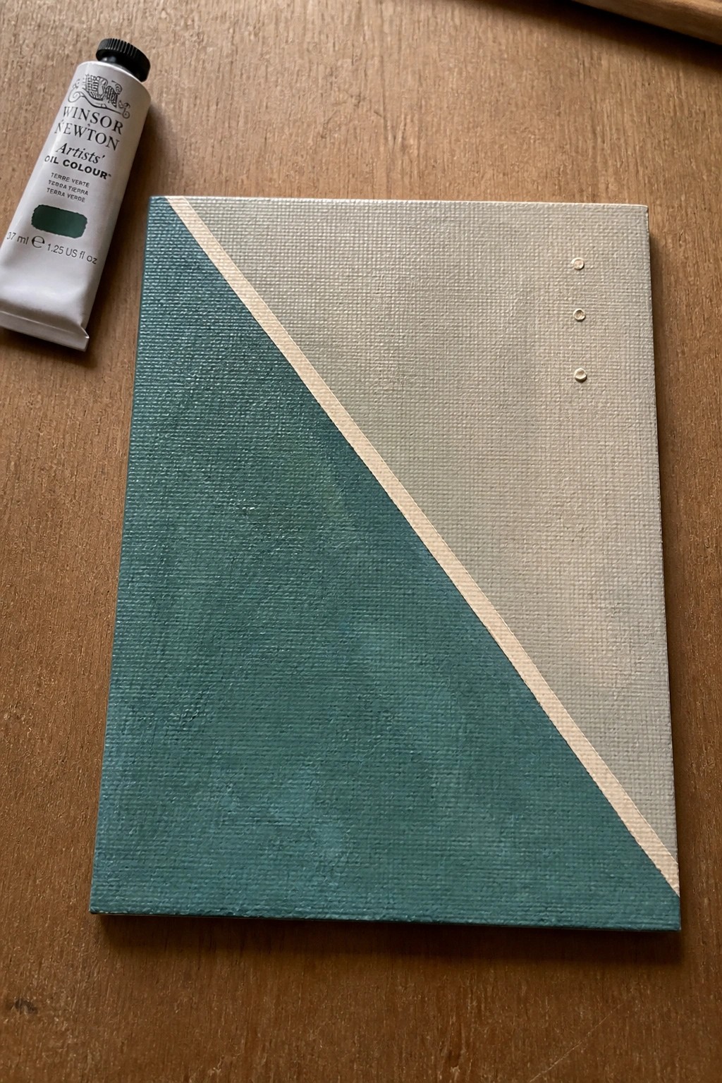 Green oil paint tube beside canvas with diagonal teal and beige halves and three dots