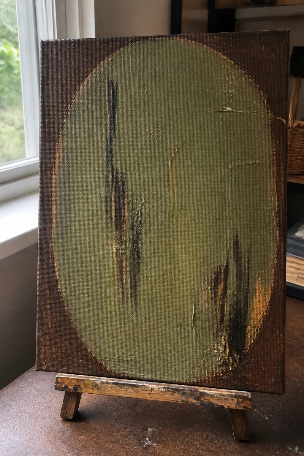 Abstract painting with green oval and dark vertical strokes on brown canvas atop wooden stand.