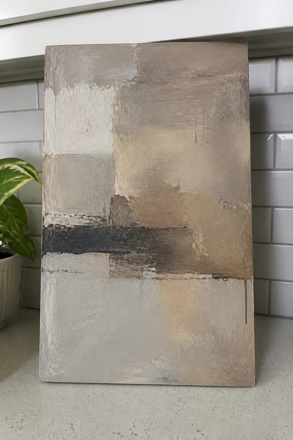 A rectangular abstract oil painting covered in textured layers of gray, beige, and white with a dark horizontal band across the lower section.