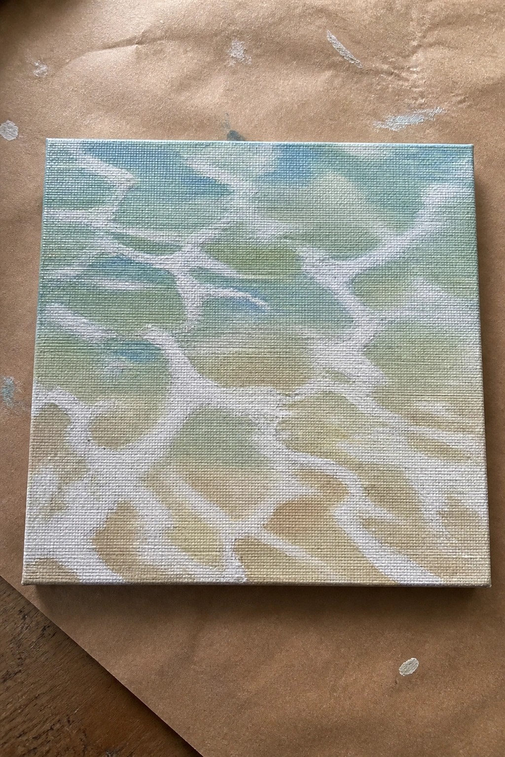 Abstract canvas with white organic shapes on blue-green-yellow gradient background on brown paper.
