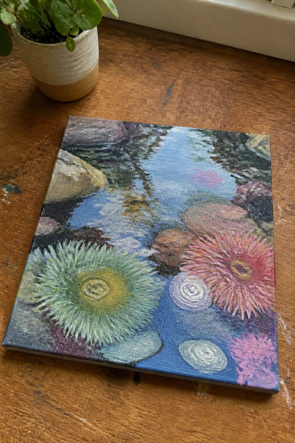 Colorful painting of underwater anemones and rocks on canvas next to potted plant