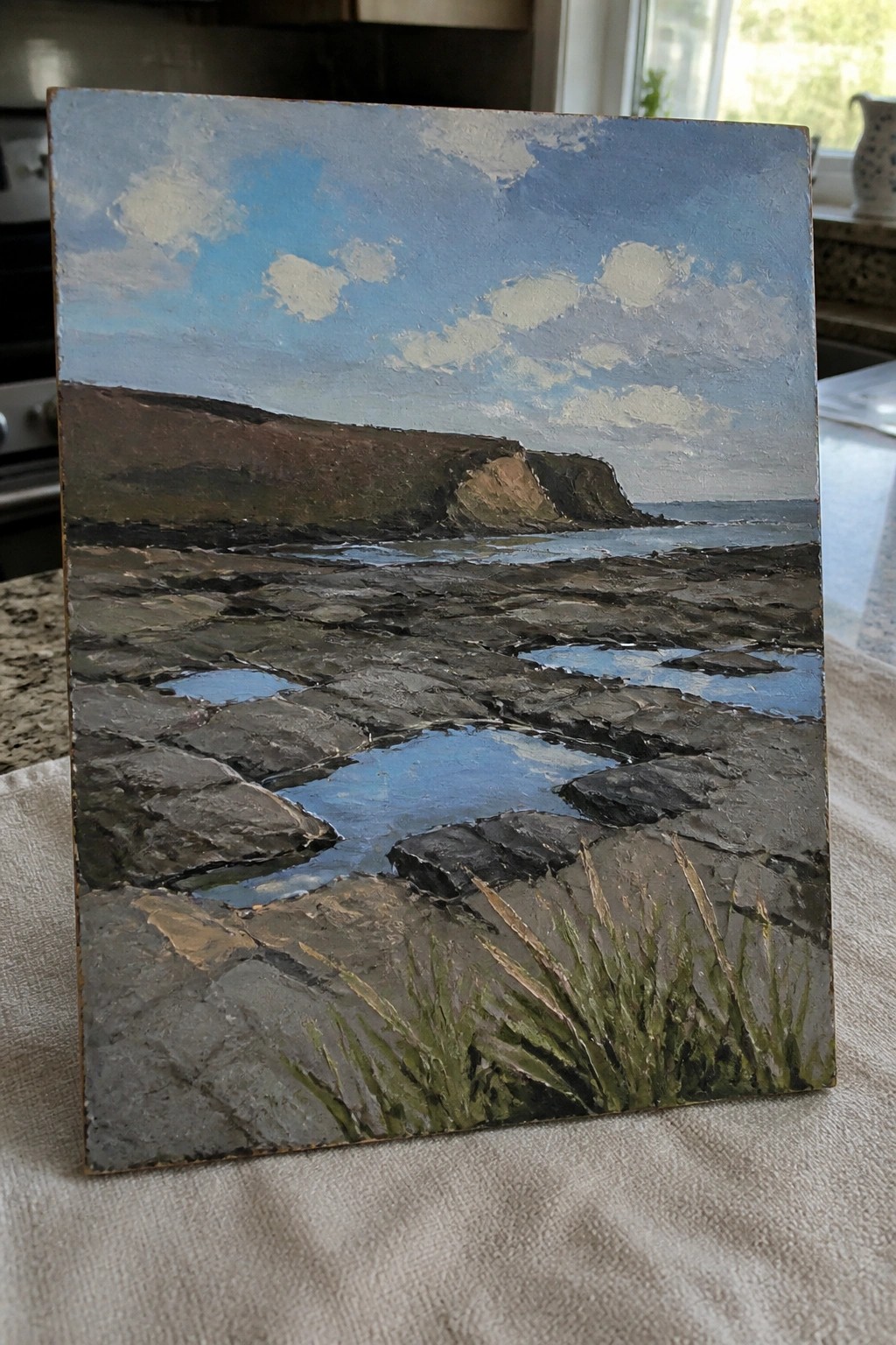 Rocky coastal landscape painting with tide pools, cliffs, and cloudy blue sky