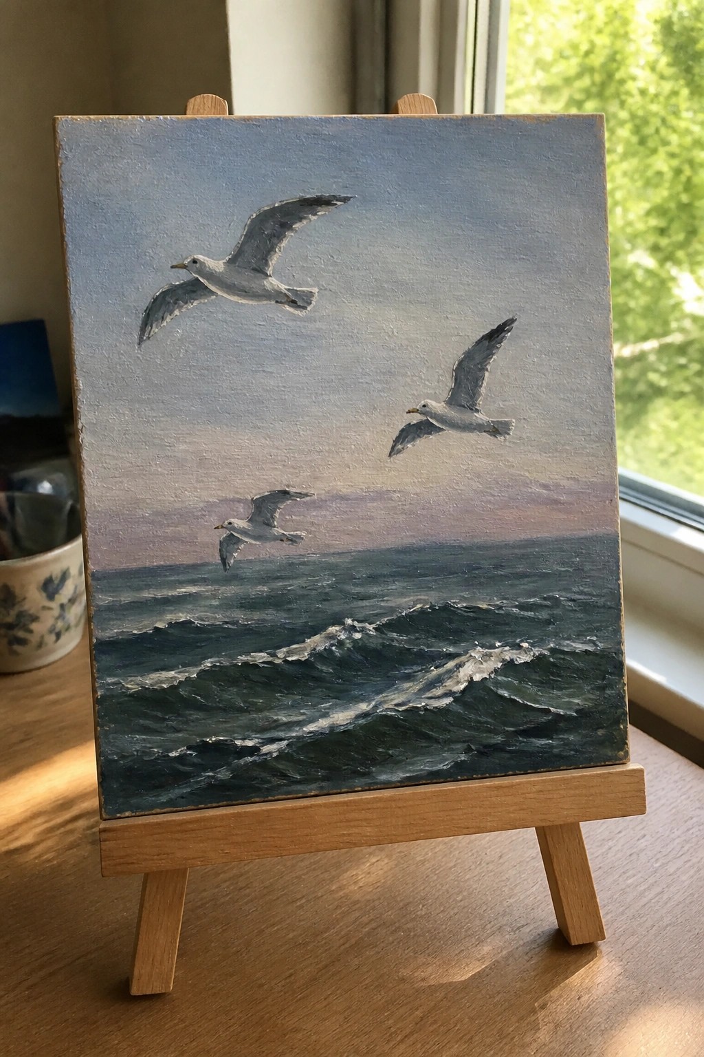 Three seagulls soar over dark wavy ocean under blue-to-pink gradient sky on easel.
