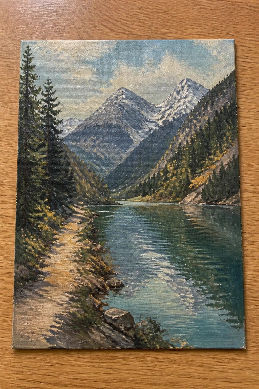 Oil painting of turquoise river winding past pine trees toward snow-capped mountains with a dirt path.