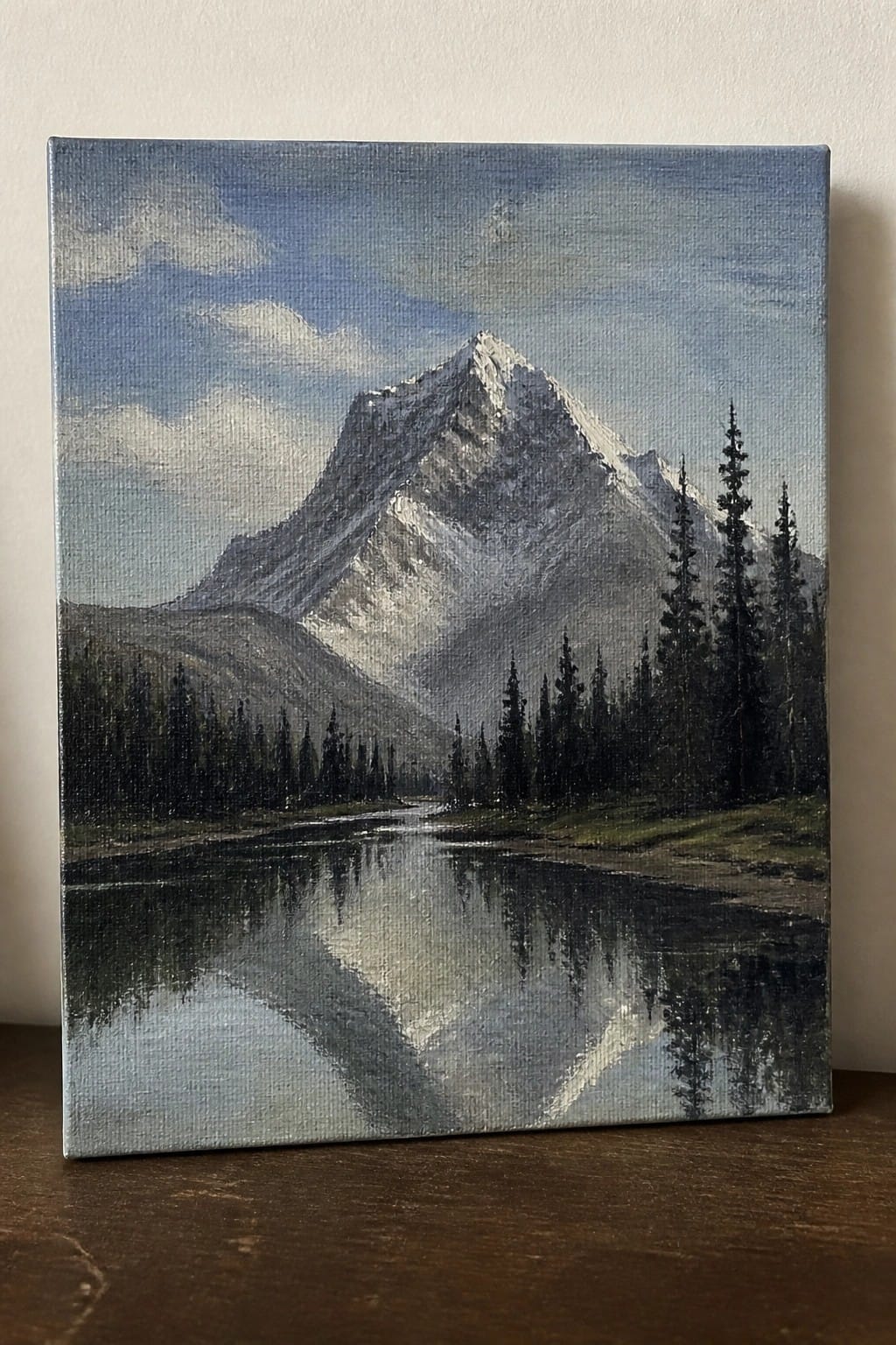 Oil painting of snow-capped mountain reflected in calm lake with pine trees