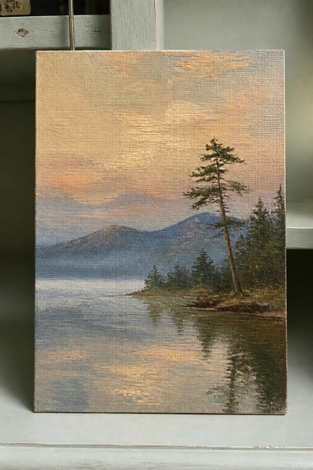 Serene canvas painting of misty mountains reflected in a lake with pine trees at sunset.