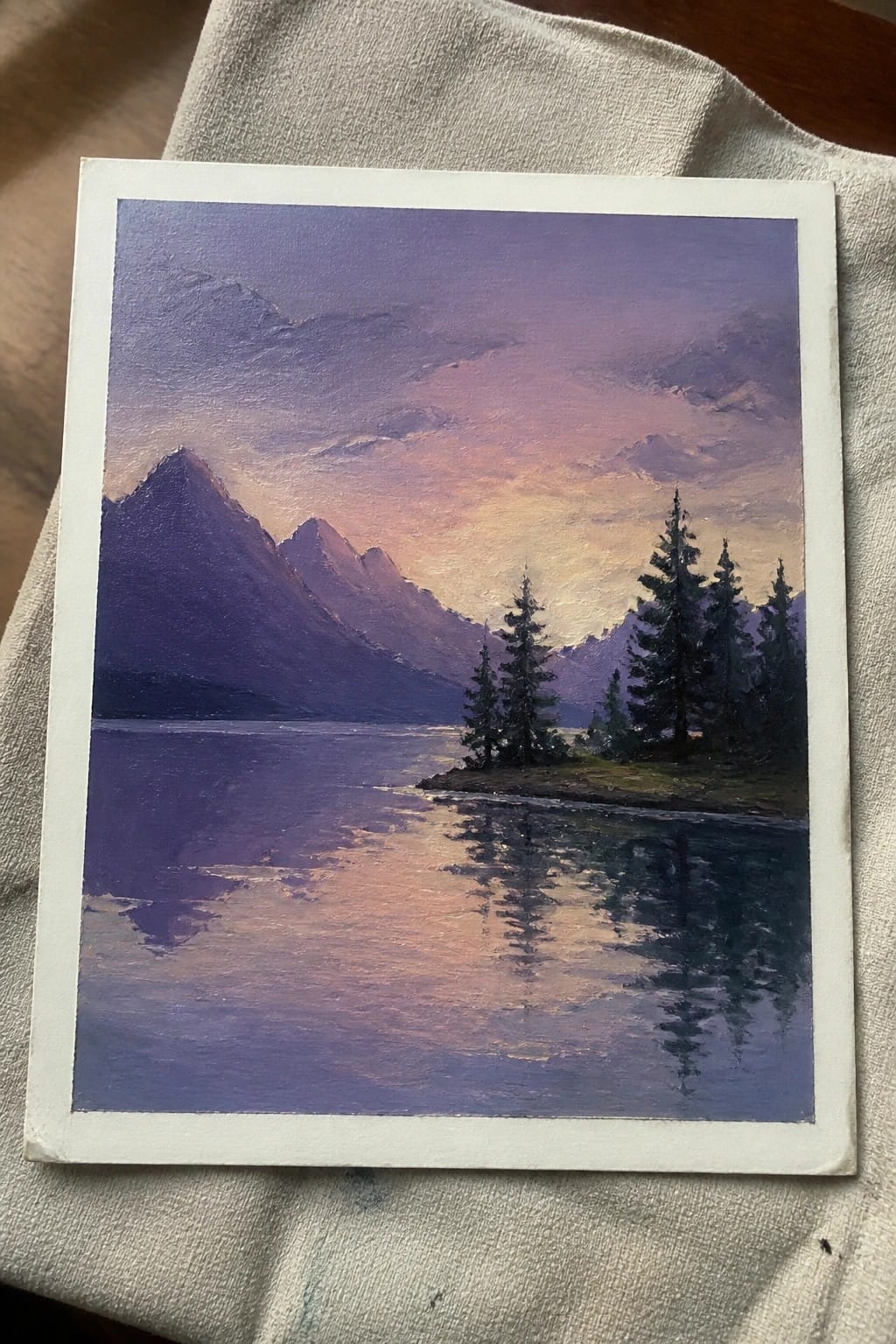 Purple-hued oil painting of mountains reflected in calm lake with pine trees at dusk