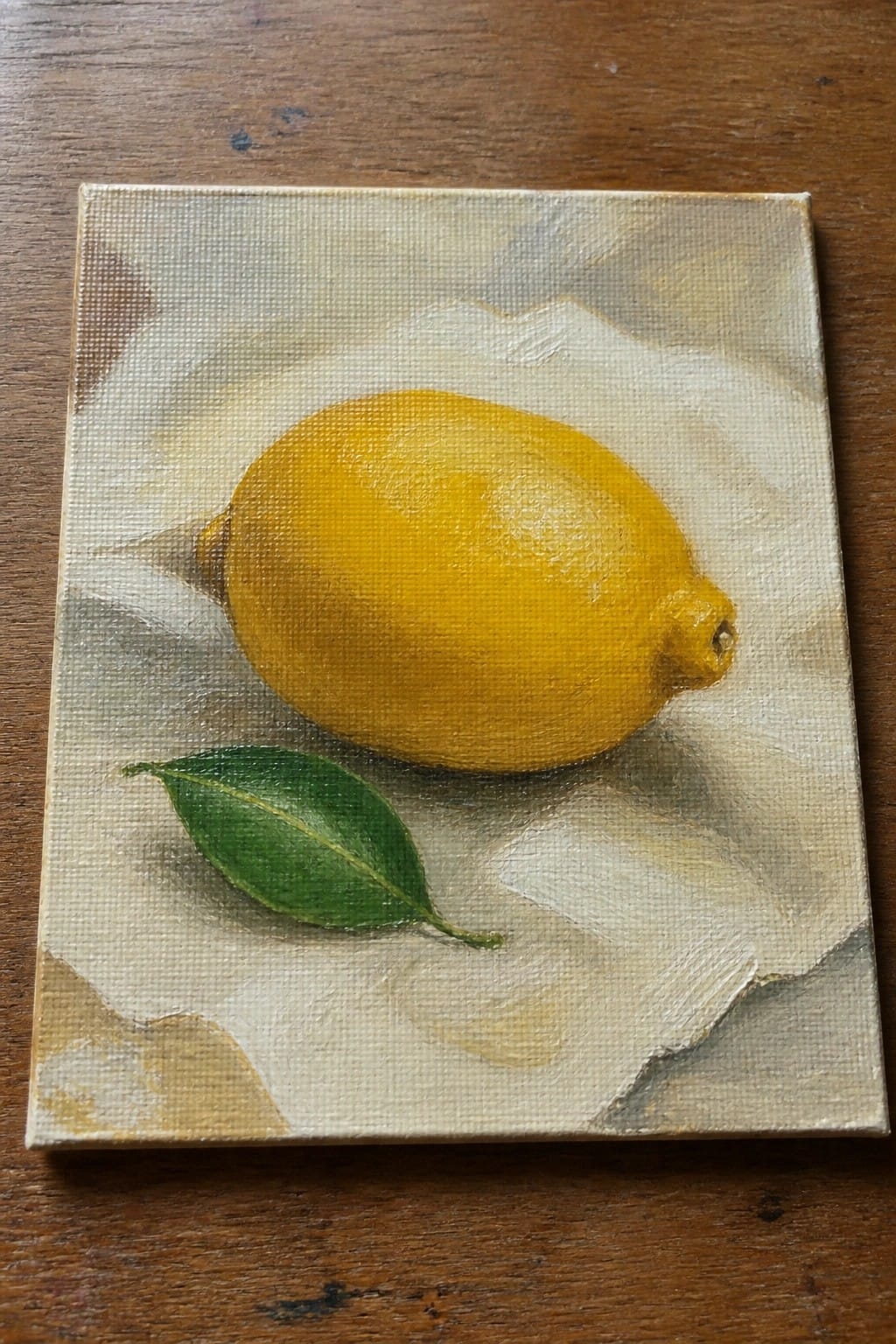 Yellow lemon with green leaf on white paper over wooden surface in oil painting