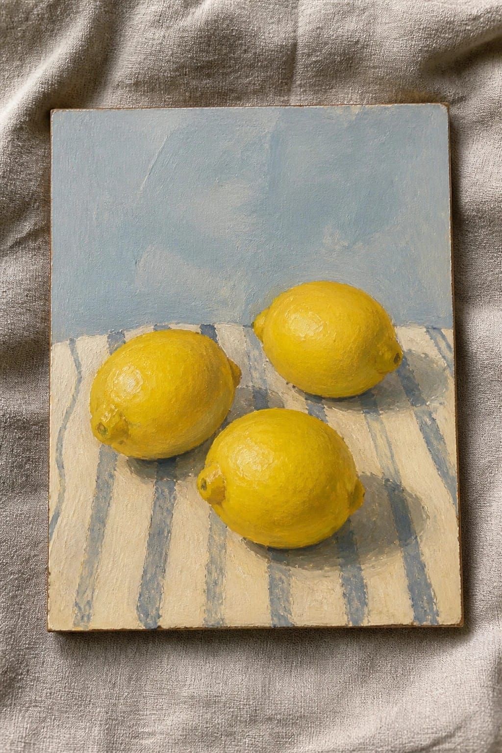 Three yellow lemons on blue-and-white striped cloth against pale blue background
