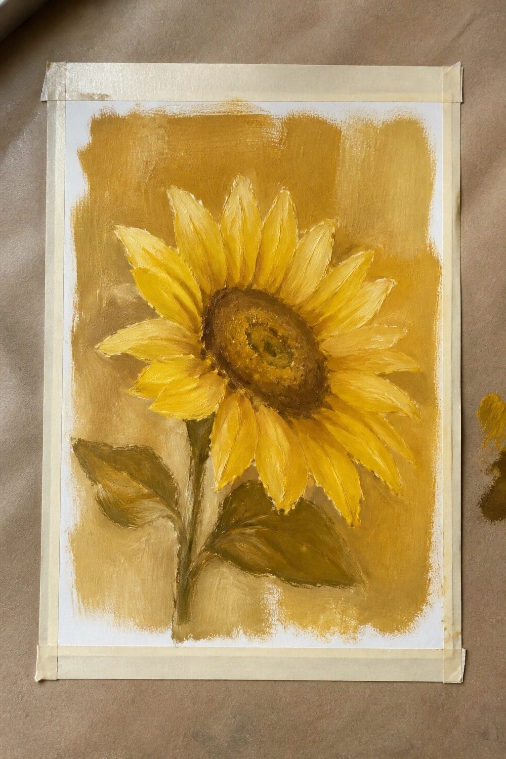 Yellow sunflower painting with brown center, green leaves, on taped paper.