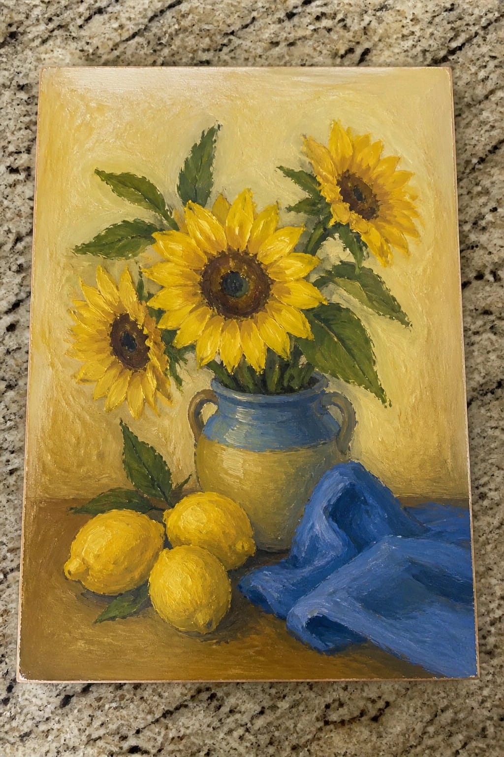 An oil painting of three sunflowers in a blue and yellow vase next to three lemons and a blue cloth on a brown surface with a yellow background.