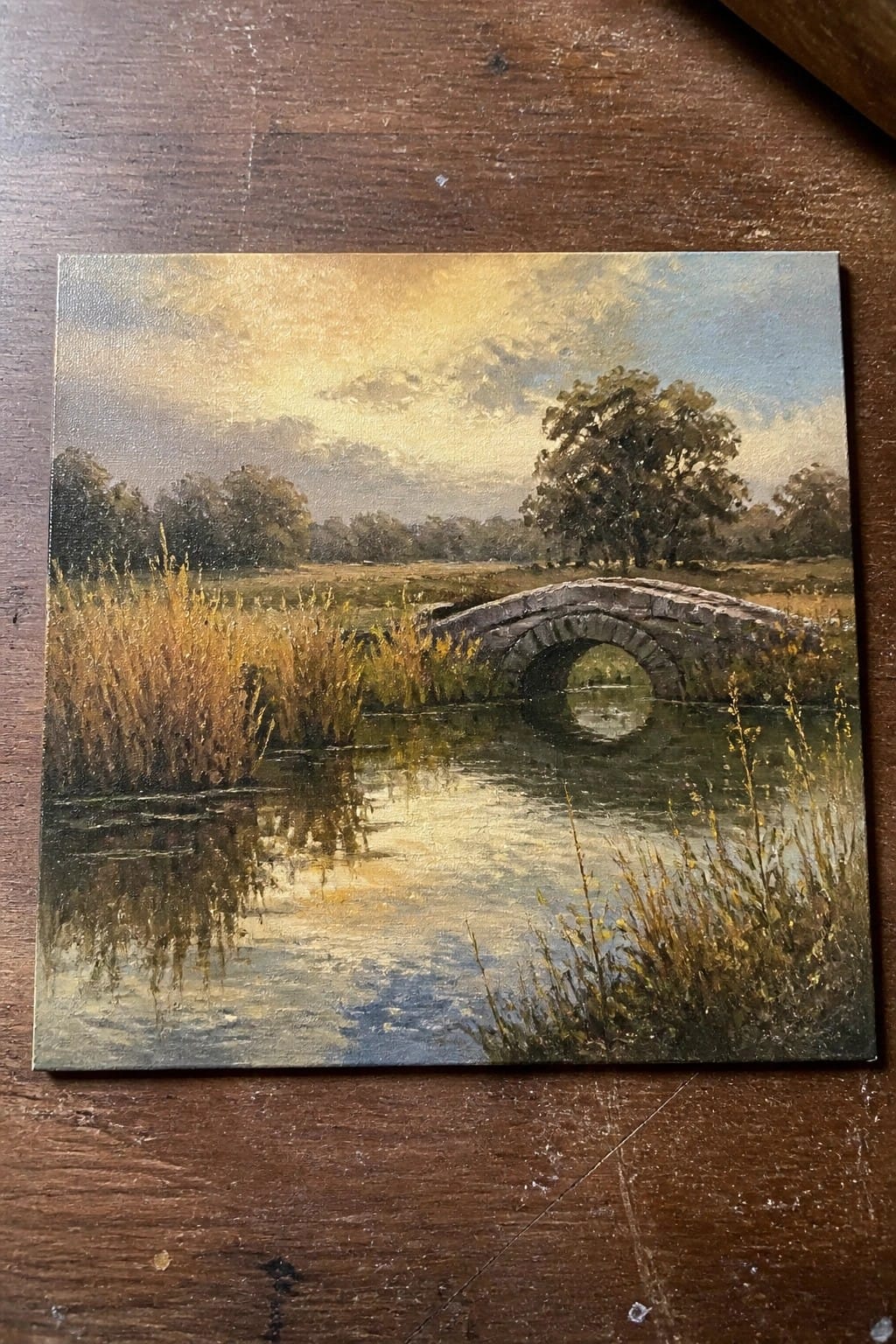 Stone bridge over reflective river at golden sunset amid tall reeds and trees.