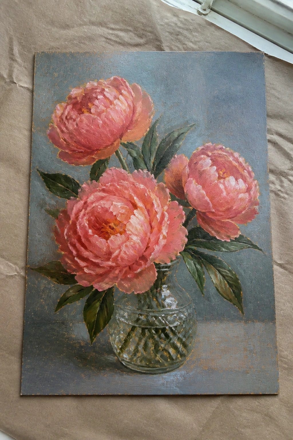 Three pink peonies with green leaves in a faceted glass vase on blue.