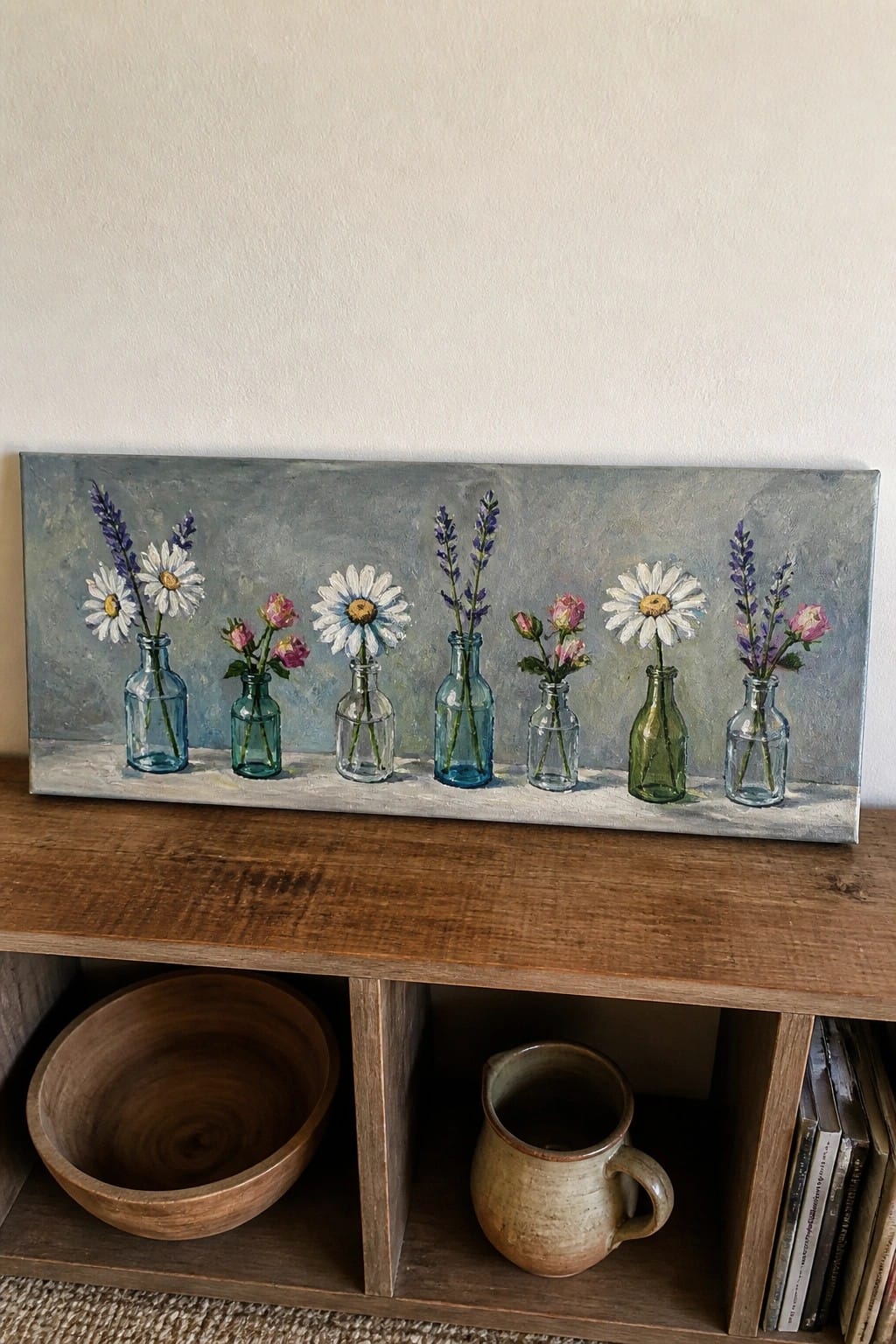 A horizontal oil painting shows seven small glass bottles with daisies, lavender, and pink roses lined up on a ledge against a muted blue-gray background.