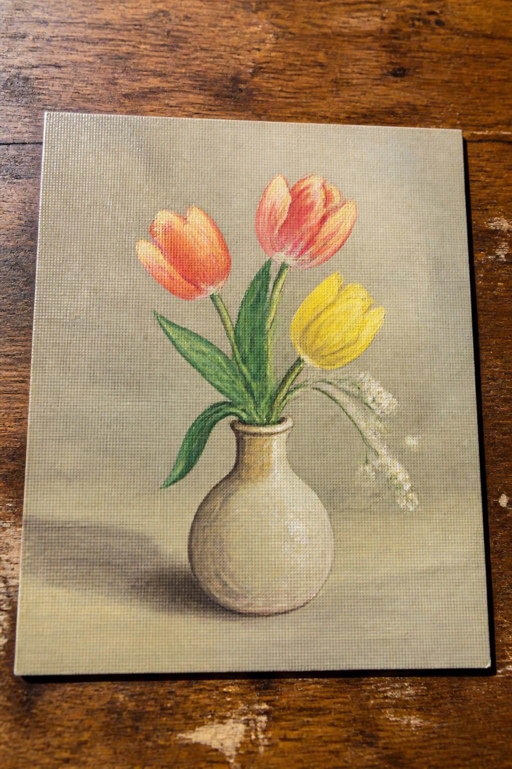 Three tulips in a beige vase on a wooden surface