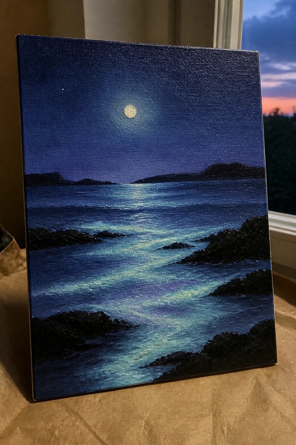Moonlit ocean painting with glowing full moon, dark rocky shores, and rippling blue waves.