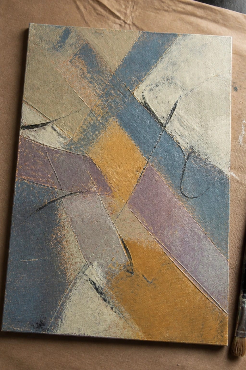 Abstract canvas with blue, gold, purple geometric shapes and paintbrush on brown surface