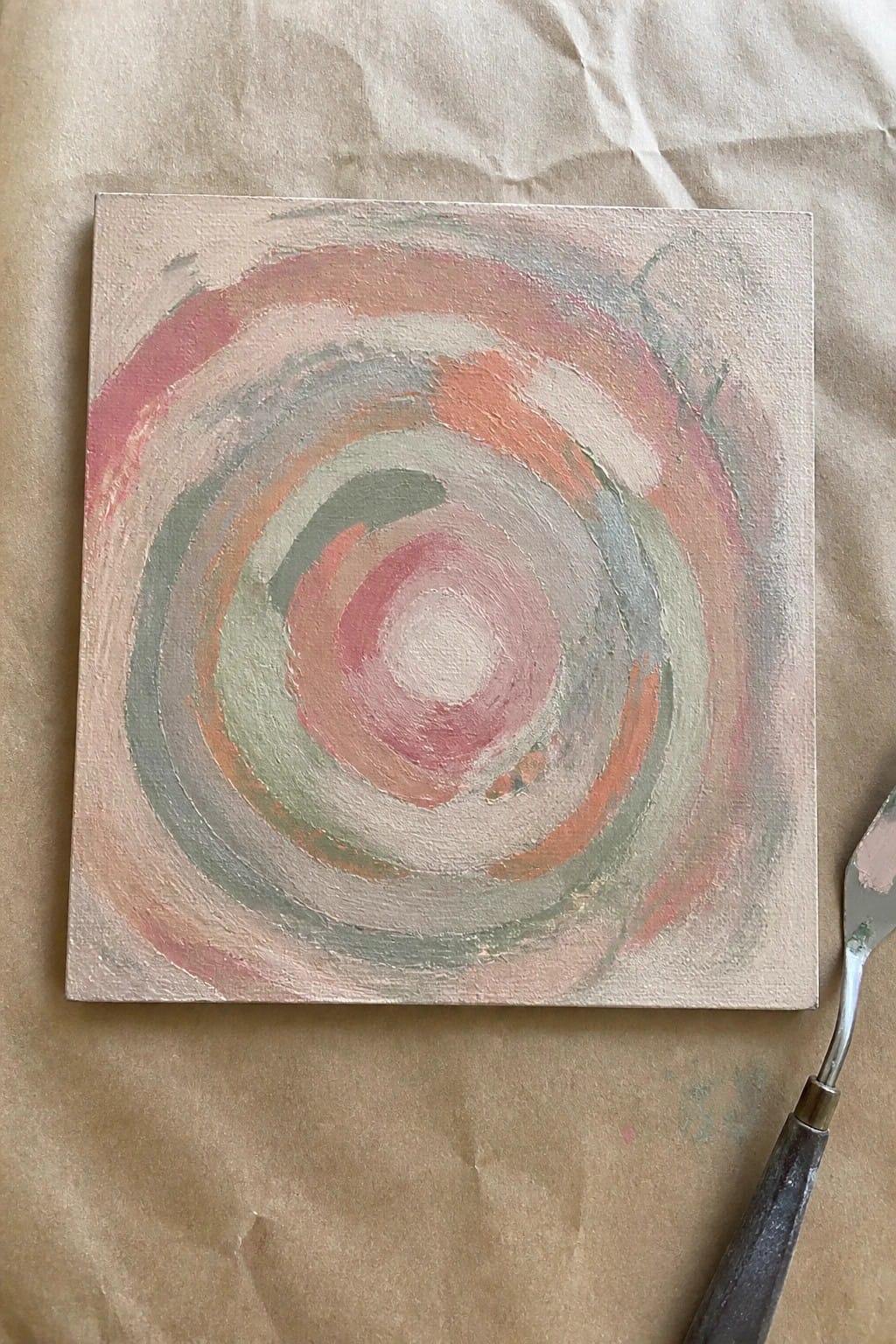 Canvas with swirling pink, orange, and green concentric circles beside a palette knife