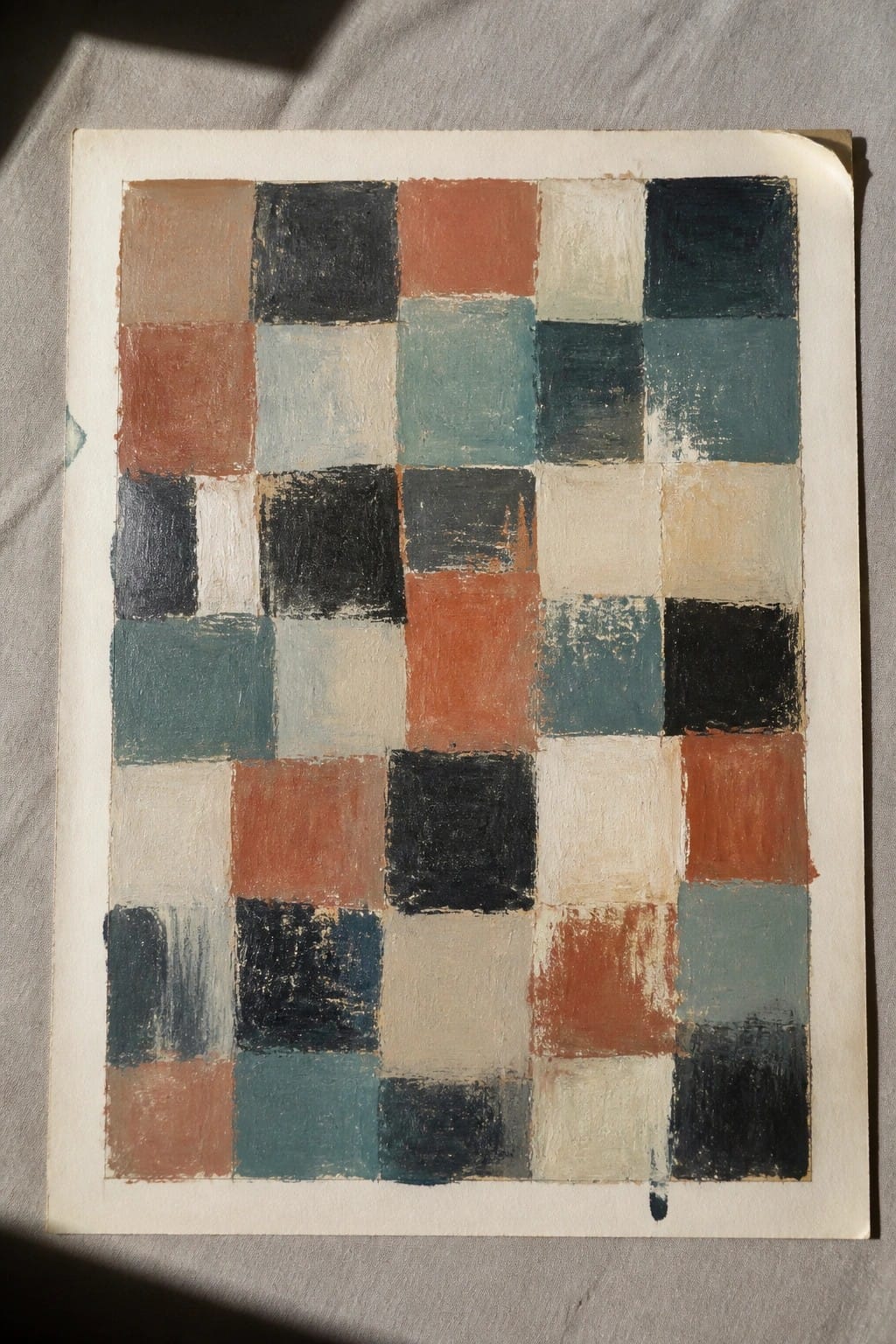 Abstract grid painting of multicolored squares in teal, orange, black, and beige on paper.