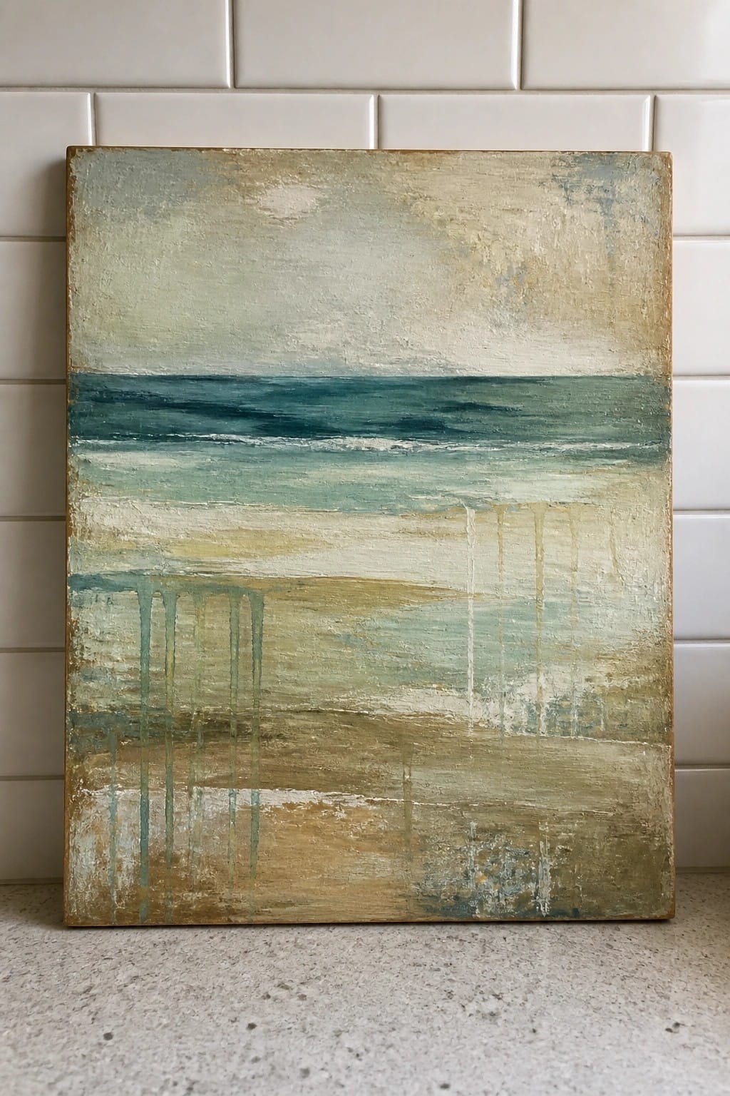 Abstract painting with layered blues, greens, and beiges leaning against white tiles