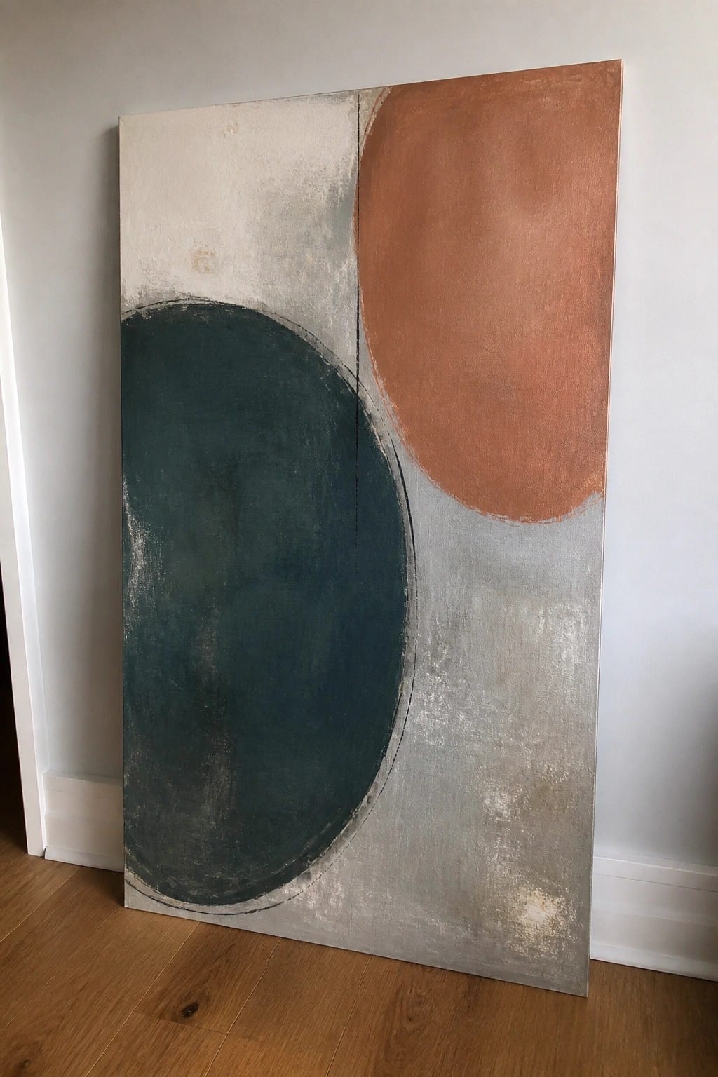 Abstract painting with large teal circle and terracotta shape against neutral background on wood floor.