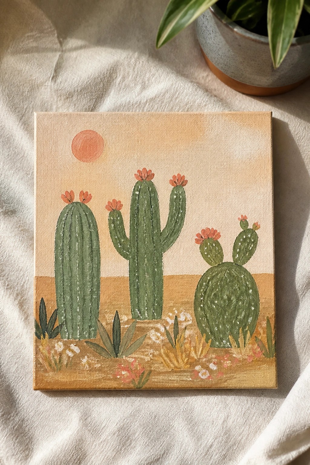 Painting of green cacti with pink flowers in desert under orange sun
