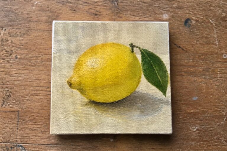 Small canvas painting of yellow lemon with green leaf on wooden table