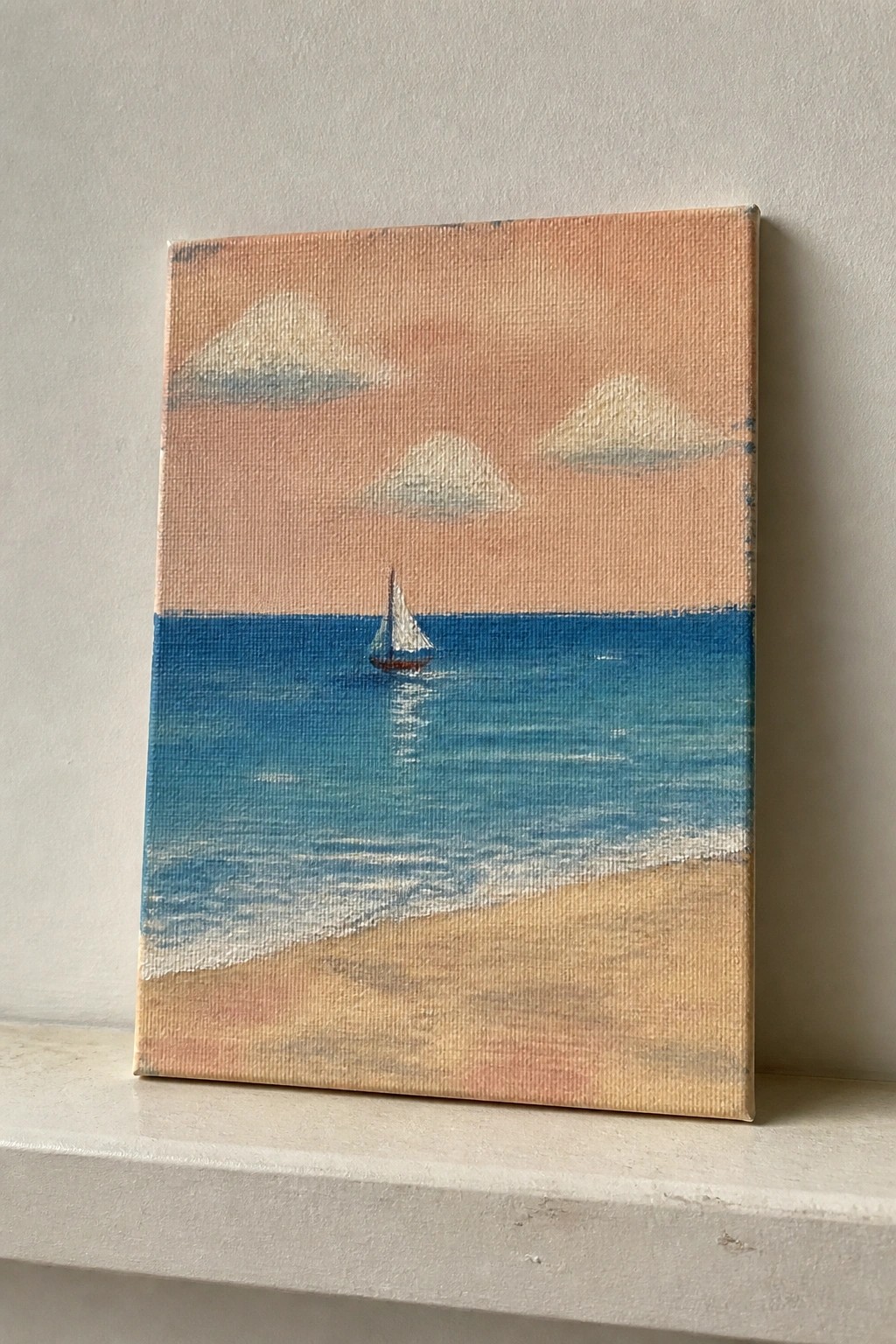 Small canvas painting of sailboat on blue ocean under pink cloudy sky on white ledge