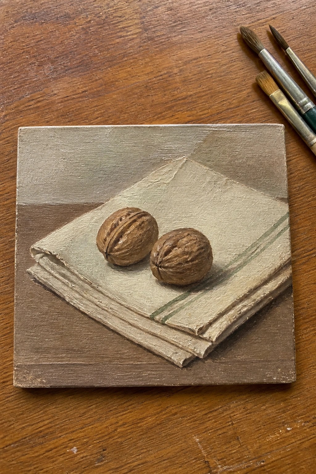 Two walnuts on a folded cloth with green stripes beside paintbrushes on wood