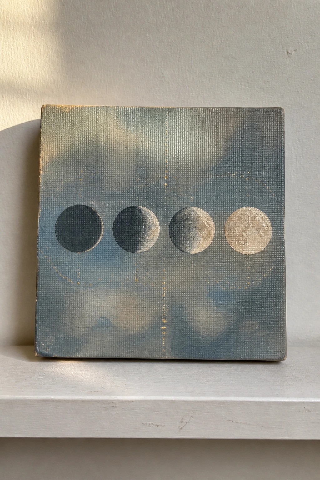 Canvas painting of four moon phases on blue cloudy background with gold speckles