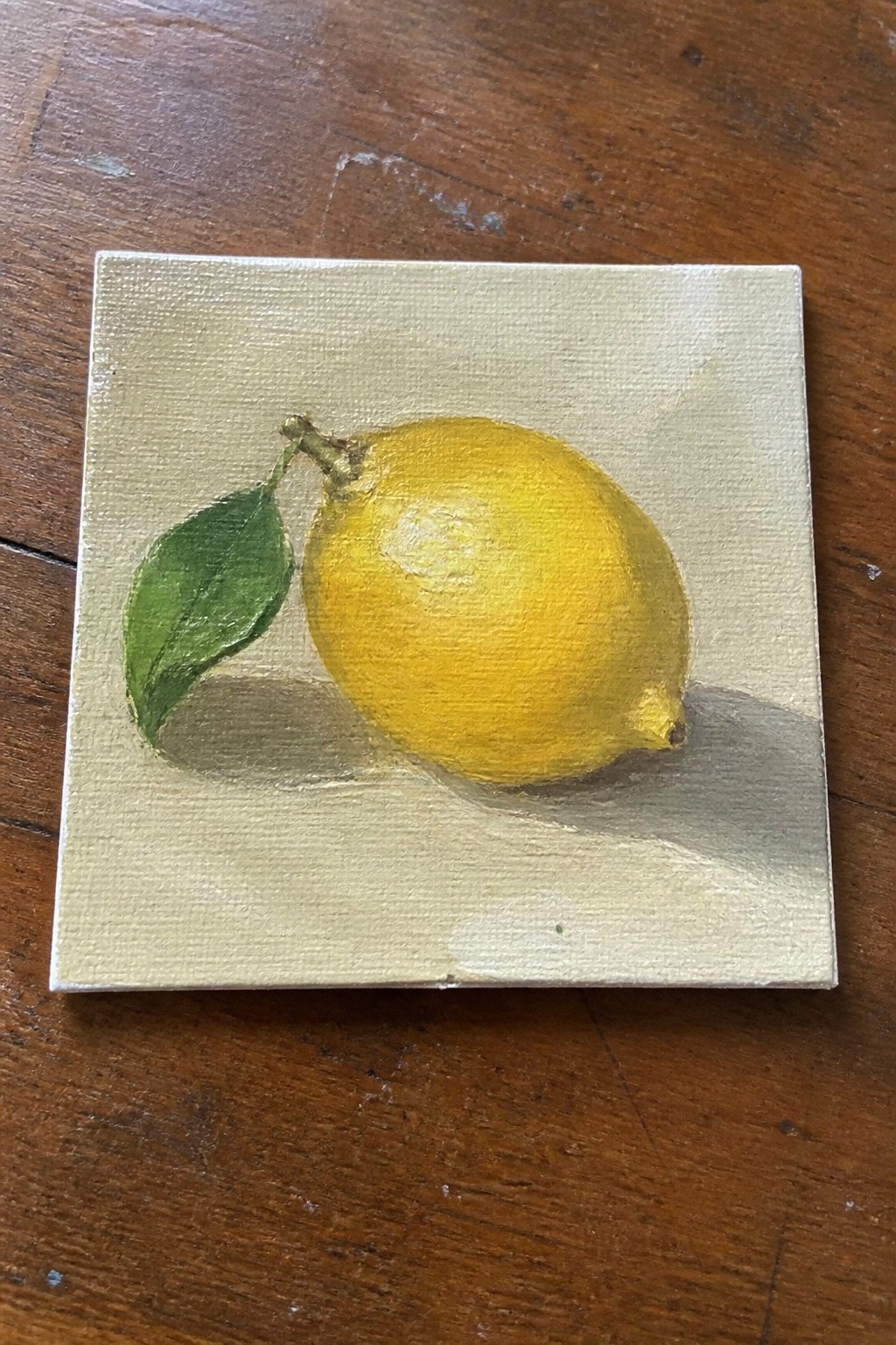 Small canvas painting of yellow lemon with green leaf on wooden table