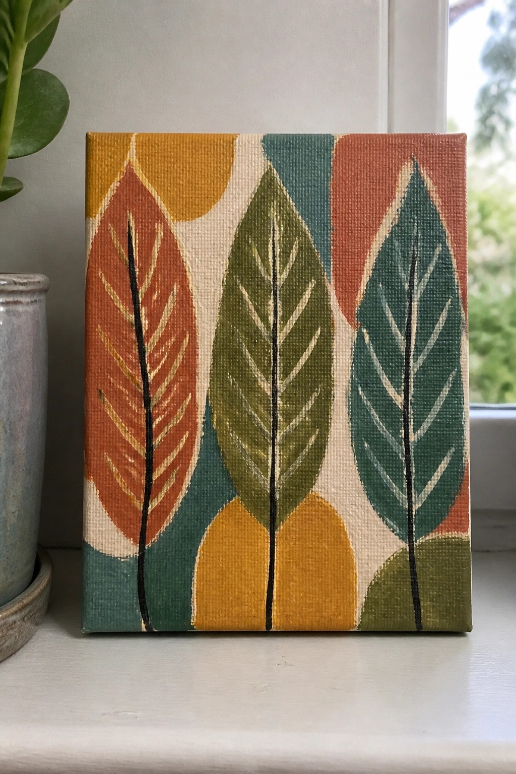 Colorful abstract canvas painting of stylized leaves in orange, green, and teal.