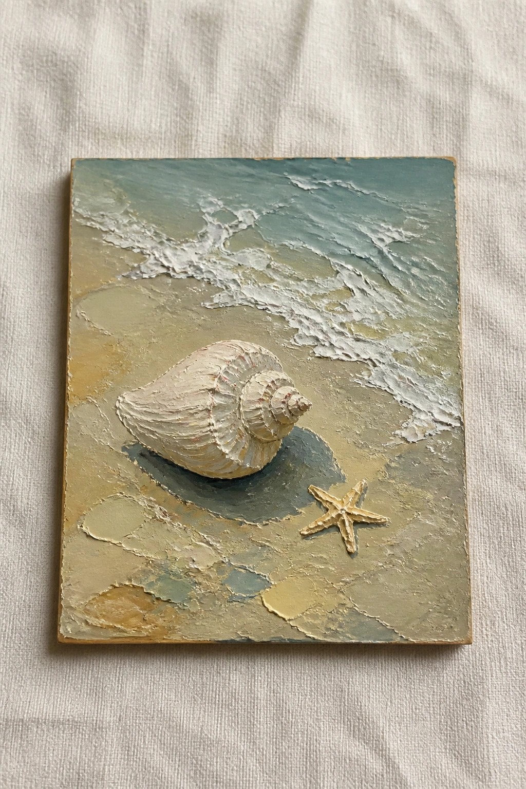 Thickly textured painting of seashell and gold starfish on beach with ocean waves
